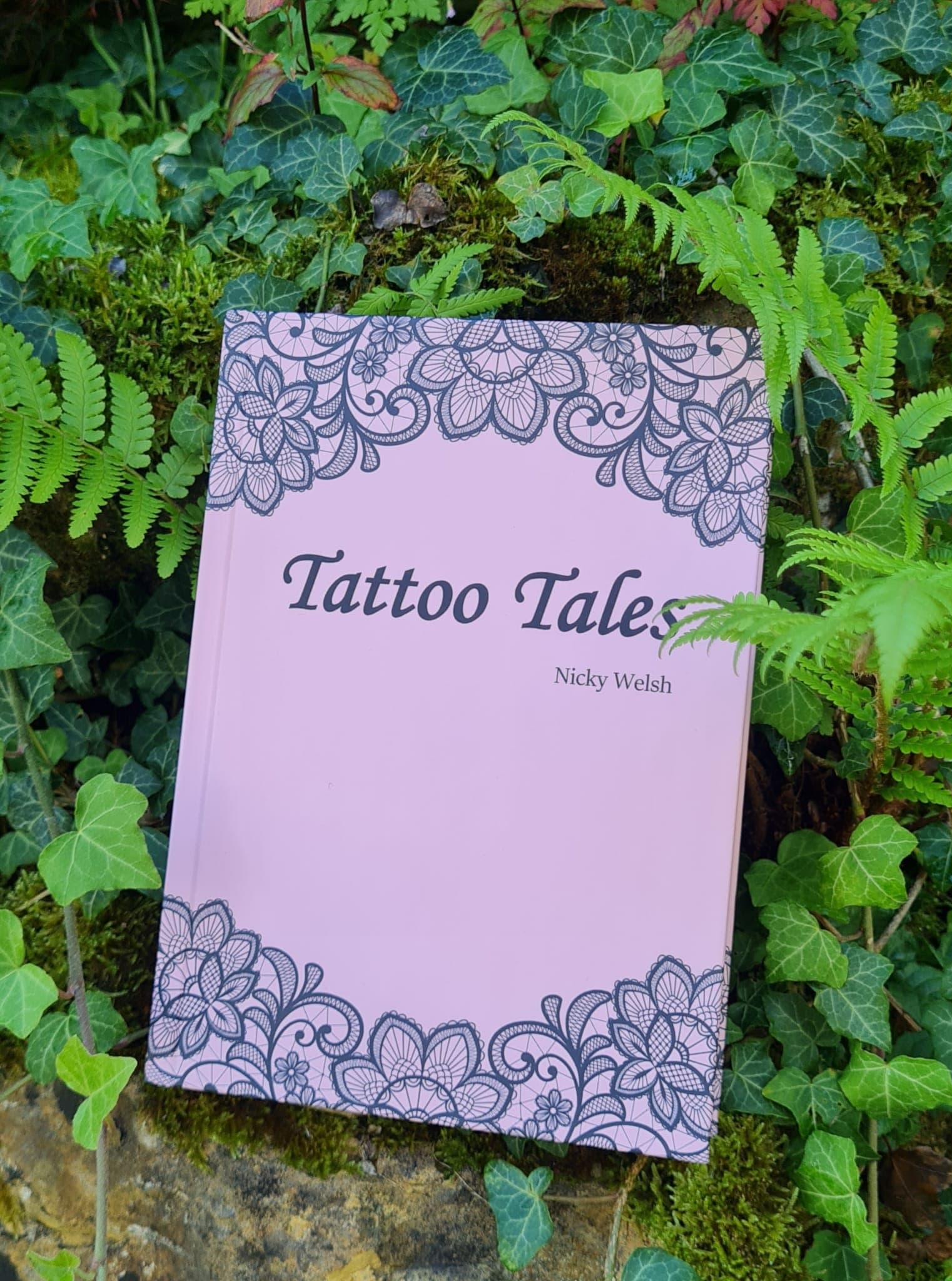 Das rosa Buch „Tattoo Tales“ steht zwischen Efeublättern